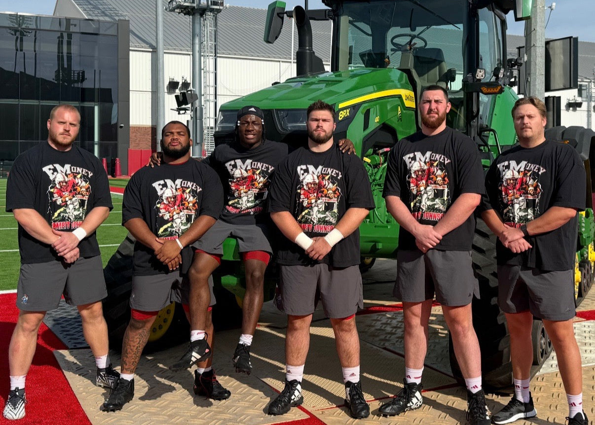 Group of men in matching outfits standing in front of a green tractor.