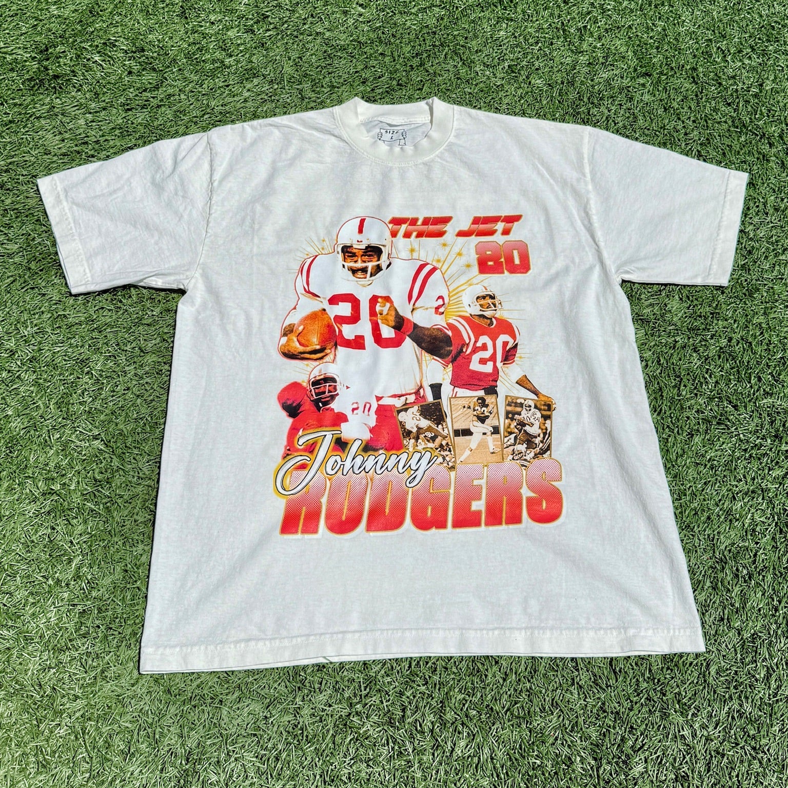 White t-shirt with football player graphics and text on a grass background