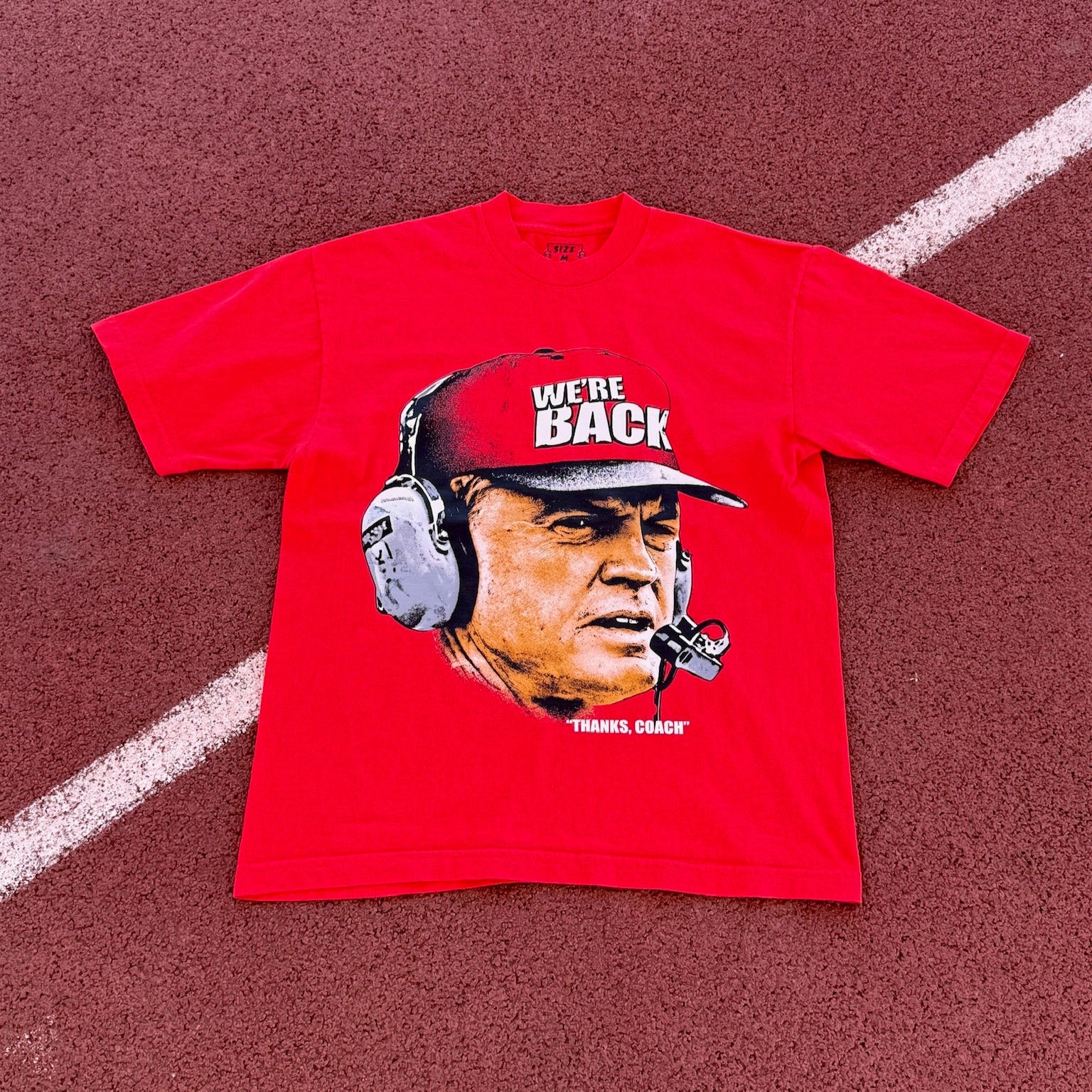 Red t-shirt with a graphic of a person wearing a helmet and 'We're Back' text on a red background