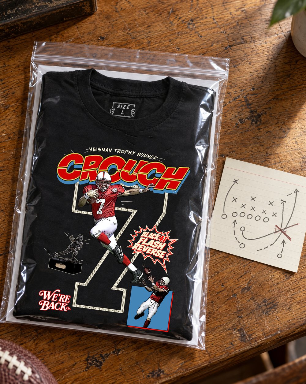 Black 41 tee folded in a clear bag on a wooden desk