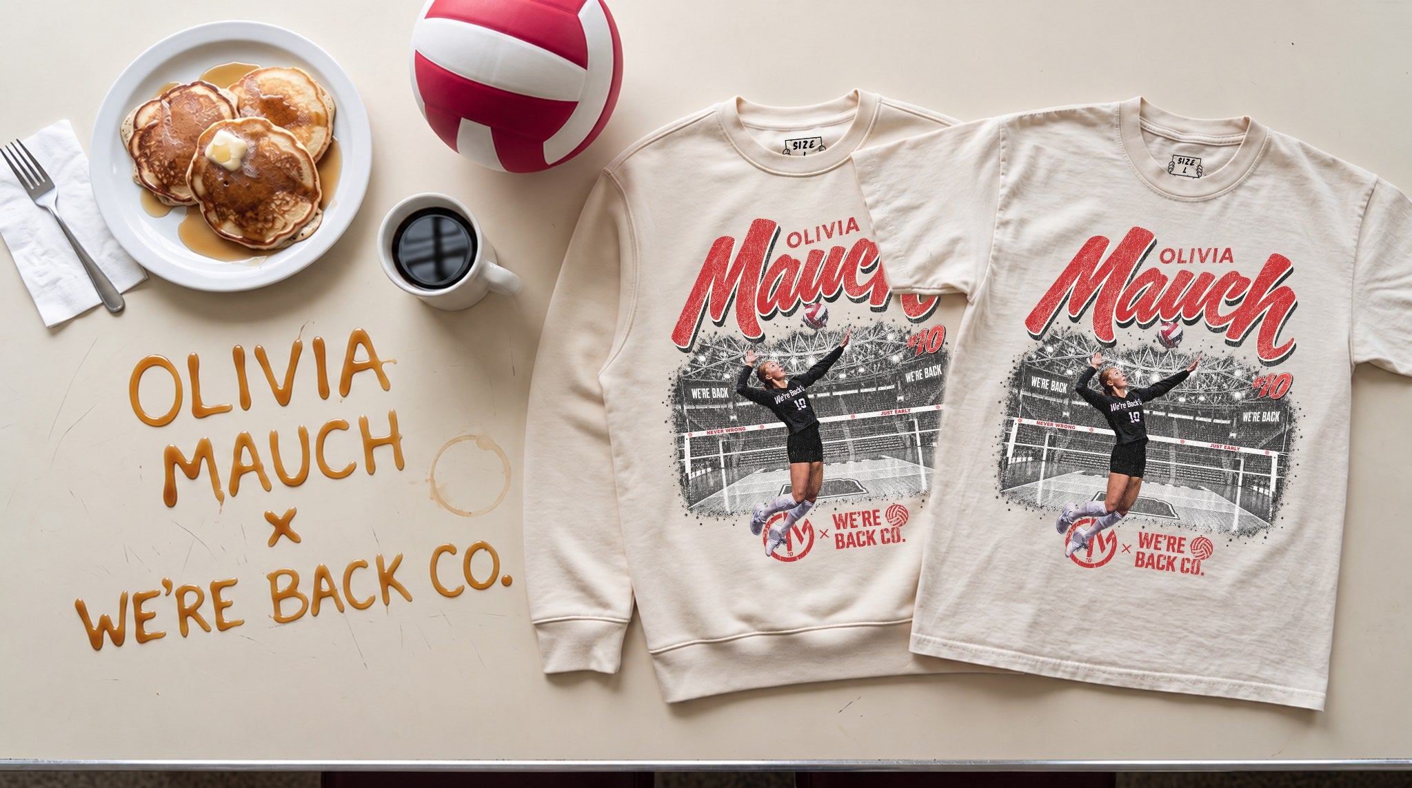 The cream crewneck and faded cream tee laid flat on a diner table next to pancakes, black coffee and a red and white volleyball, with Olivia Mauch × We're Back Co. written in syrup.
