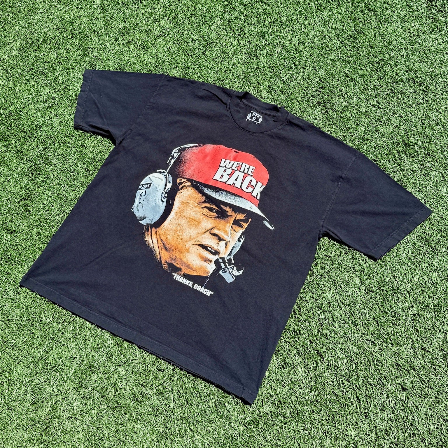 Black t-shirt with a graphic of a person wearing a red cap and headphones on grass.