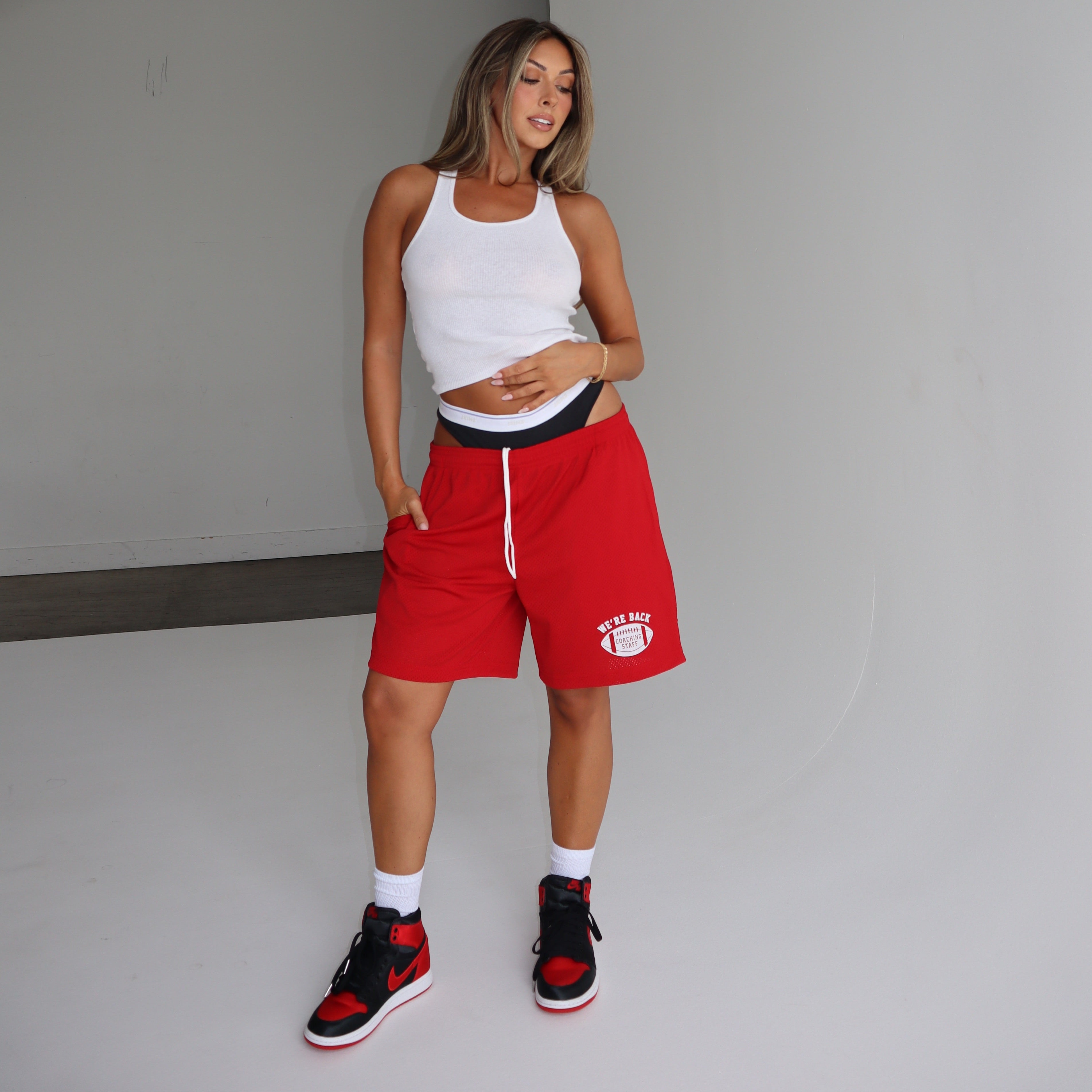 Woman wearing a white tank top and red shorts standing in a minimalistic room.