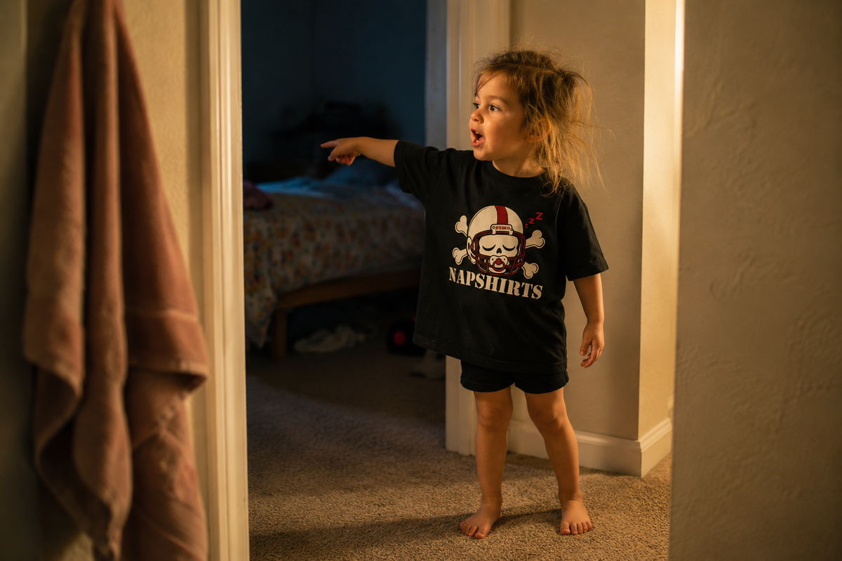 Toddler in the Napshirts toddler tee, stalling bedtime in a hallway doorway