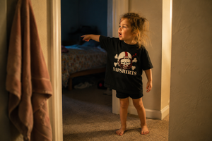 Toddler in the Napshirts toddler tee, stalling bedtime in a hallway doorway