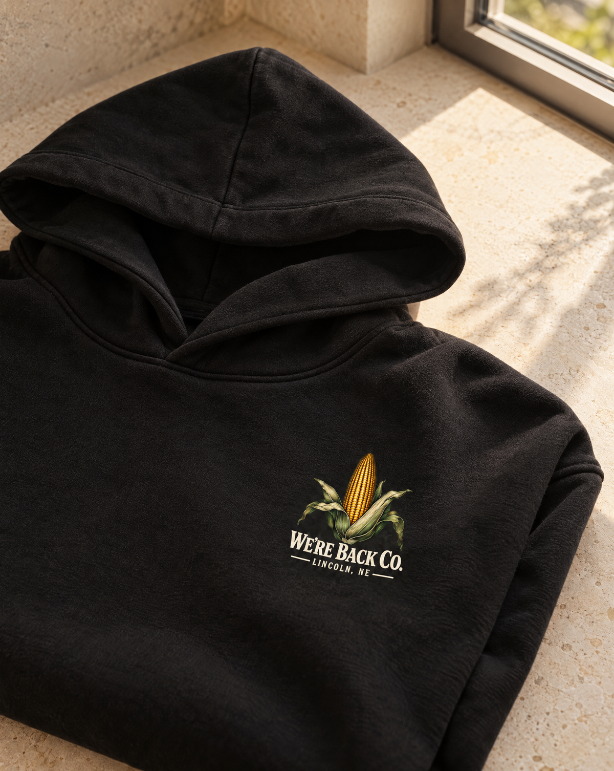 Close-up of the corn and cream WE’RE BACK CO. chest print on the True Black hoodie
