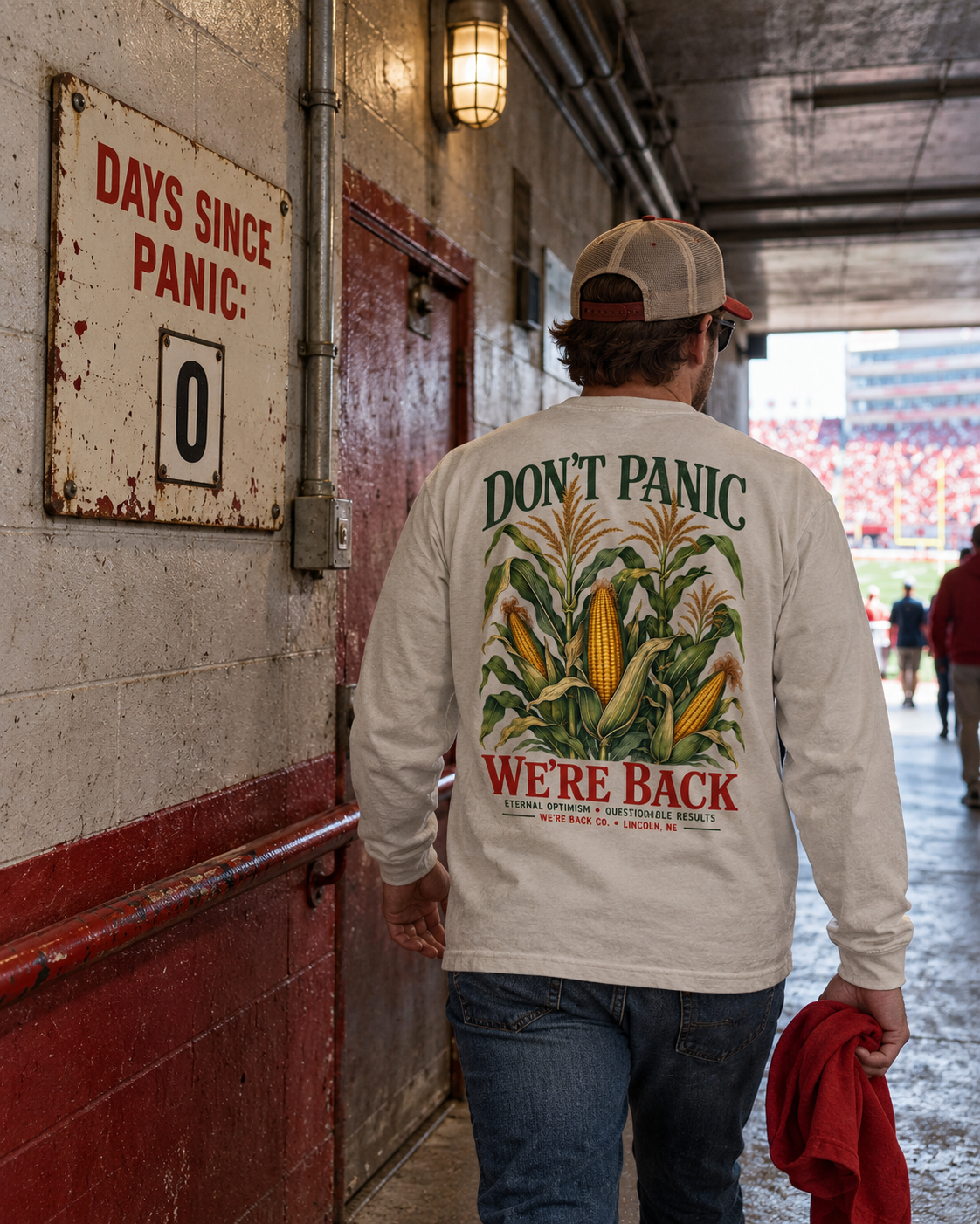 Fan wearing the Don't Panic long sleeve beside a Days Since Panic sign in a stadium tunnel.
