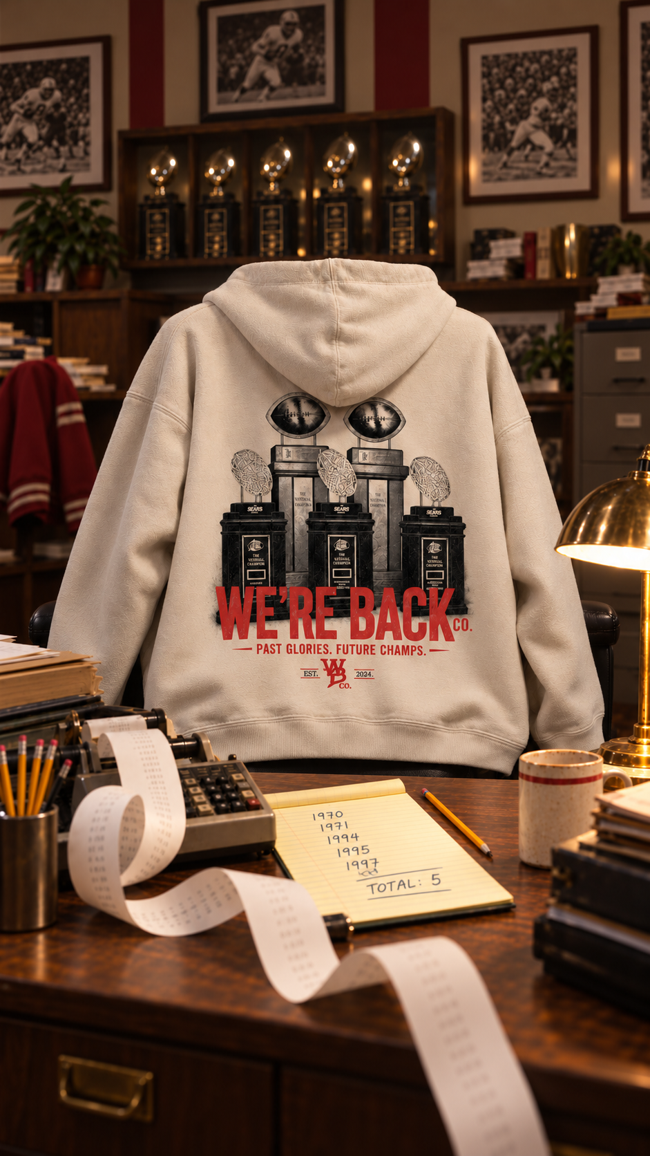 Natural Trophy Hoodie on a chair beside an adding machine and a ledger counting five titles.